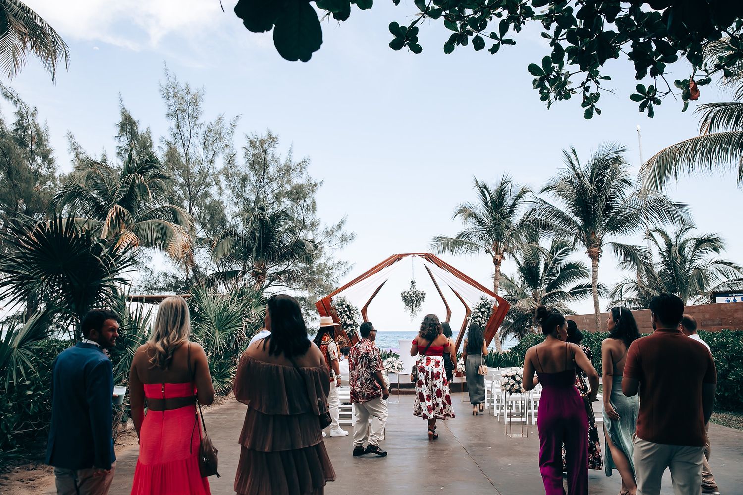 Tropical outdoor wedding ceremony setup with palm trees and white chairs under a blue sky.