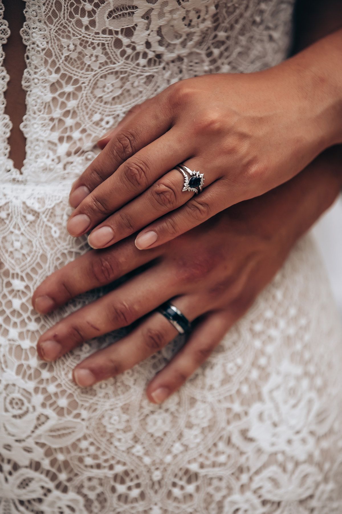 Close-up shots of hands wearing engagement rings resting on white lace fabric showing wedding day details.