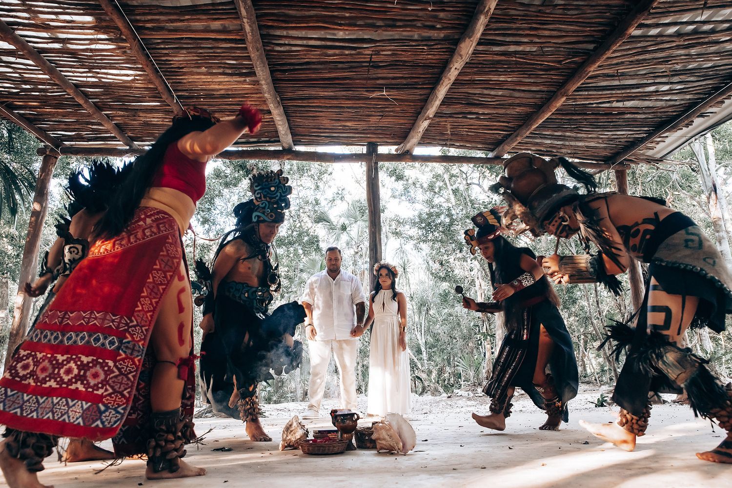People dance and celebrate under a rustic wooden pergola in an outdoor setting.