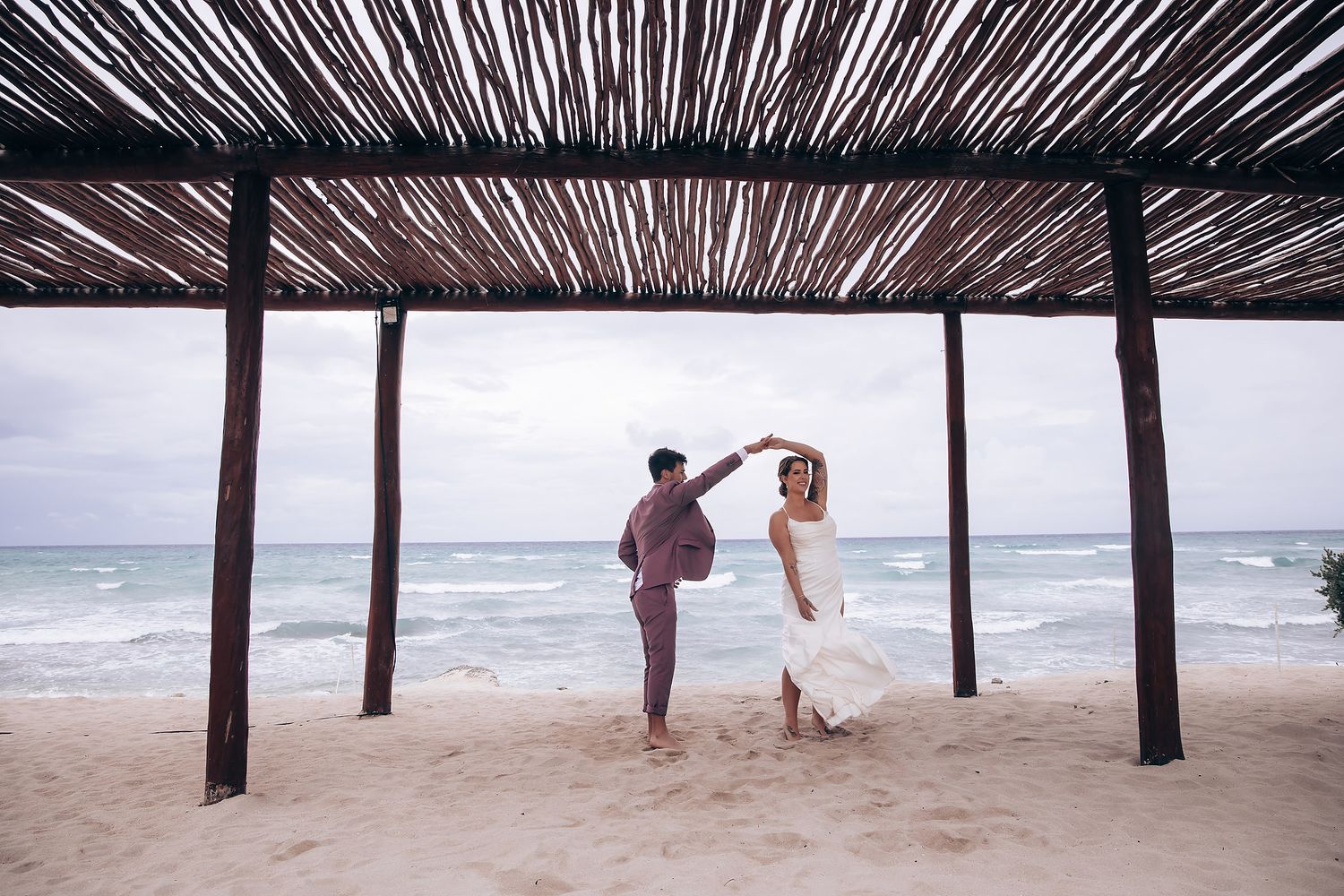 Beach wedding venue with thatched palm roof and ocean view.