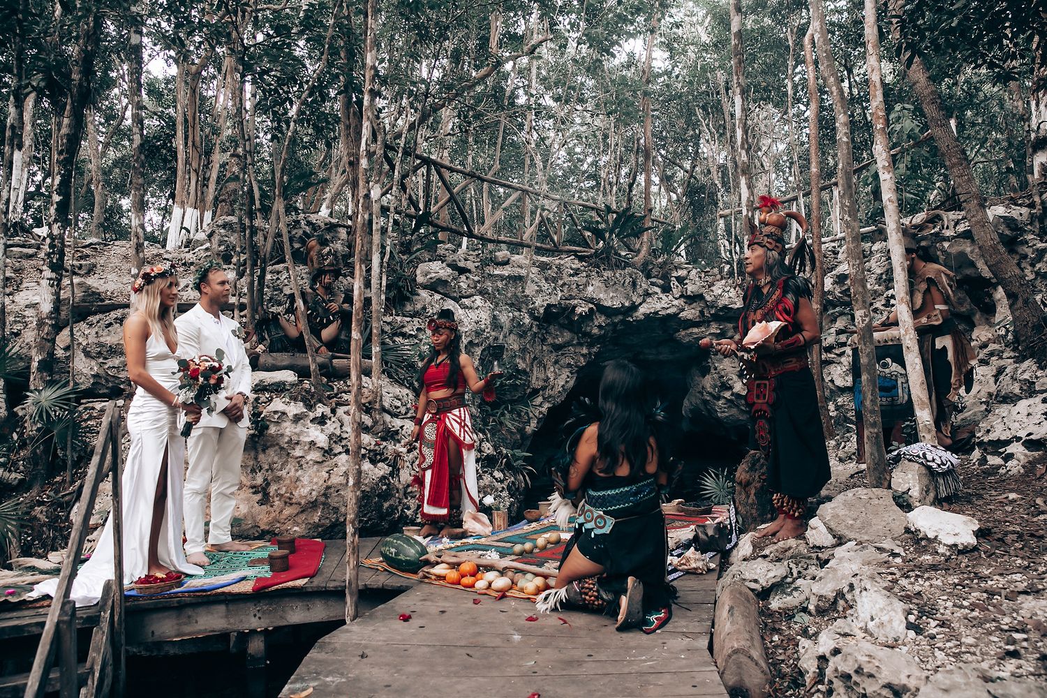 Outdoor forest wedding ceremony with guests seated on wooden benches among trees.