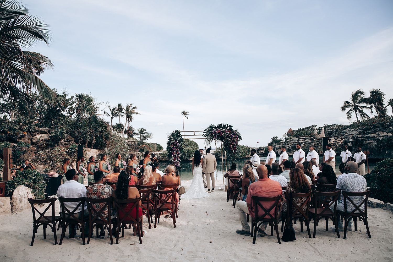 Beach wedding ceremony setup with chairs and palm trees against blue sky.