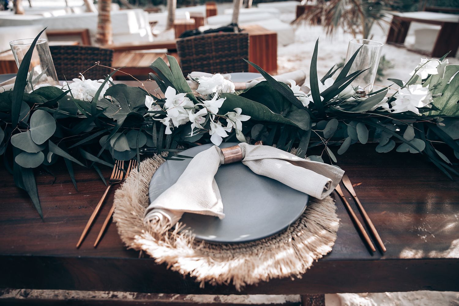 Elegant place setting with eucalyptus and white floral decorations on rustic wooden table.