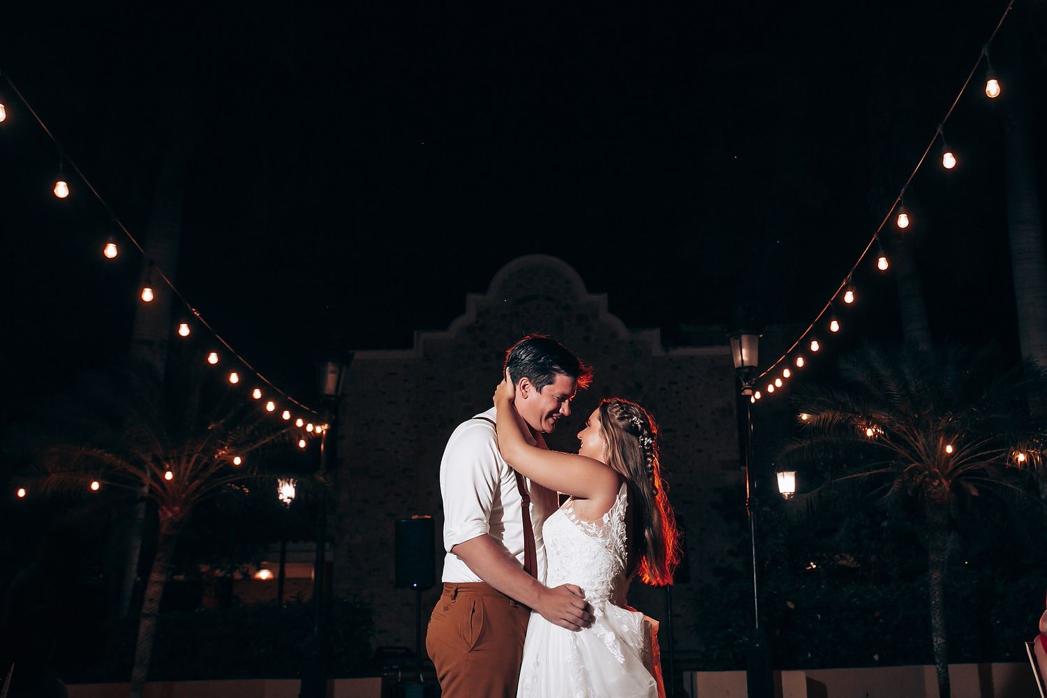 Wedding celebration under string lights with guests dancing at night.
