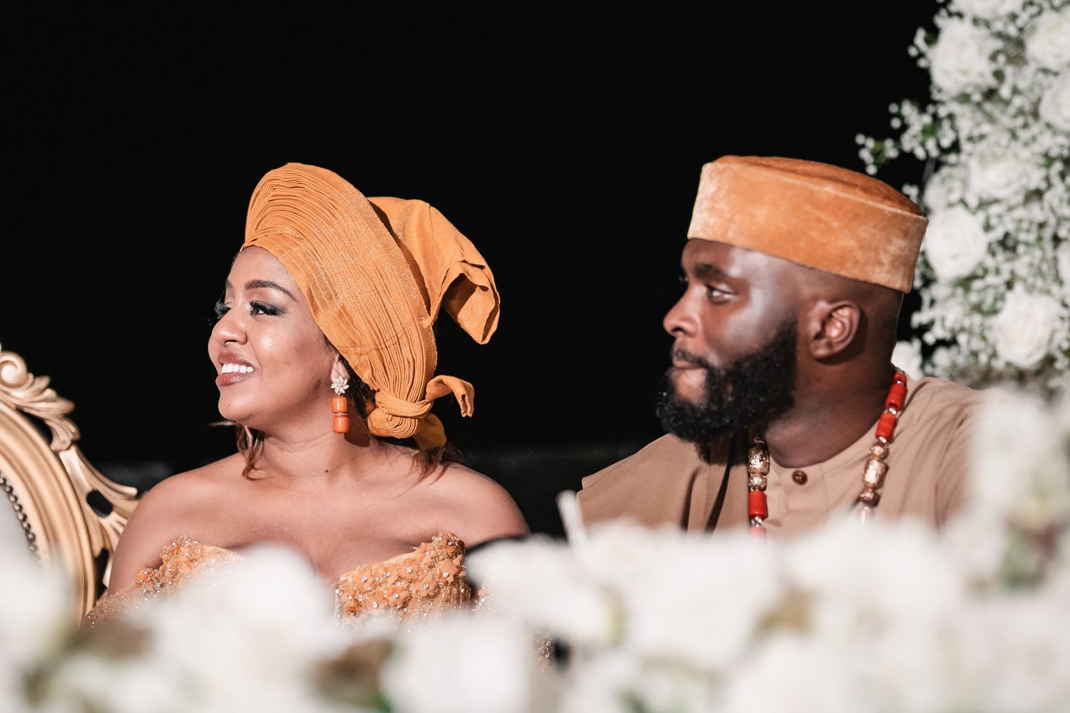 Couple in traditional African wedding attire with golden headwrap and beaded accessories.