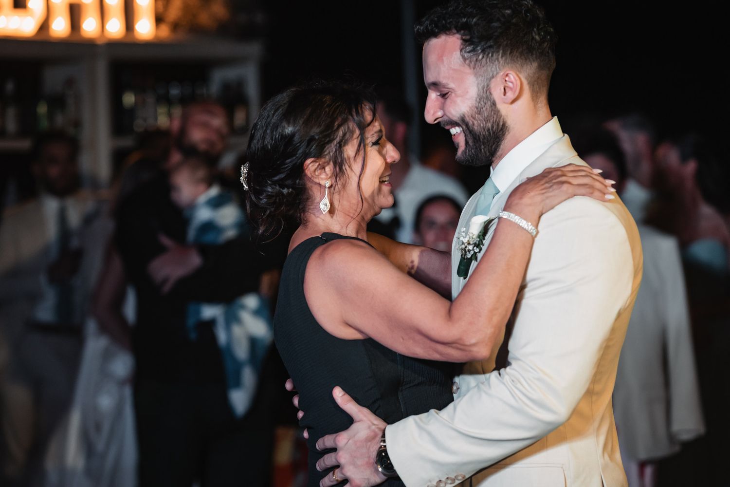 Groom sharing joyful mother-son dance with woman in black dress at wedding reception.