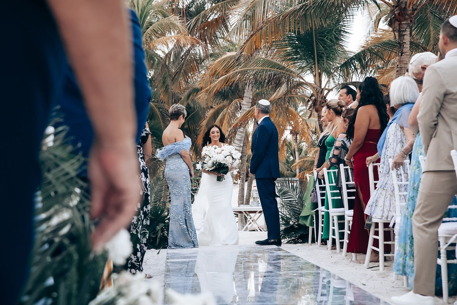 Wedding guests seated in white chairs during an outdoor tropical ceremony.