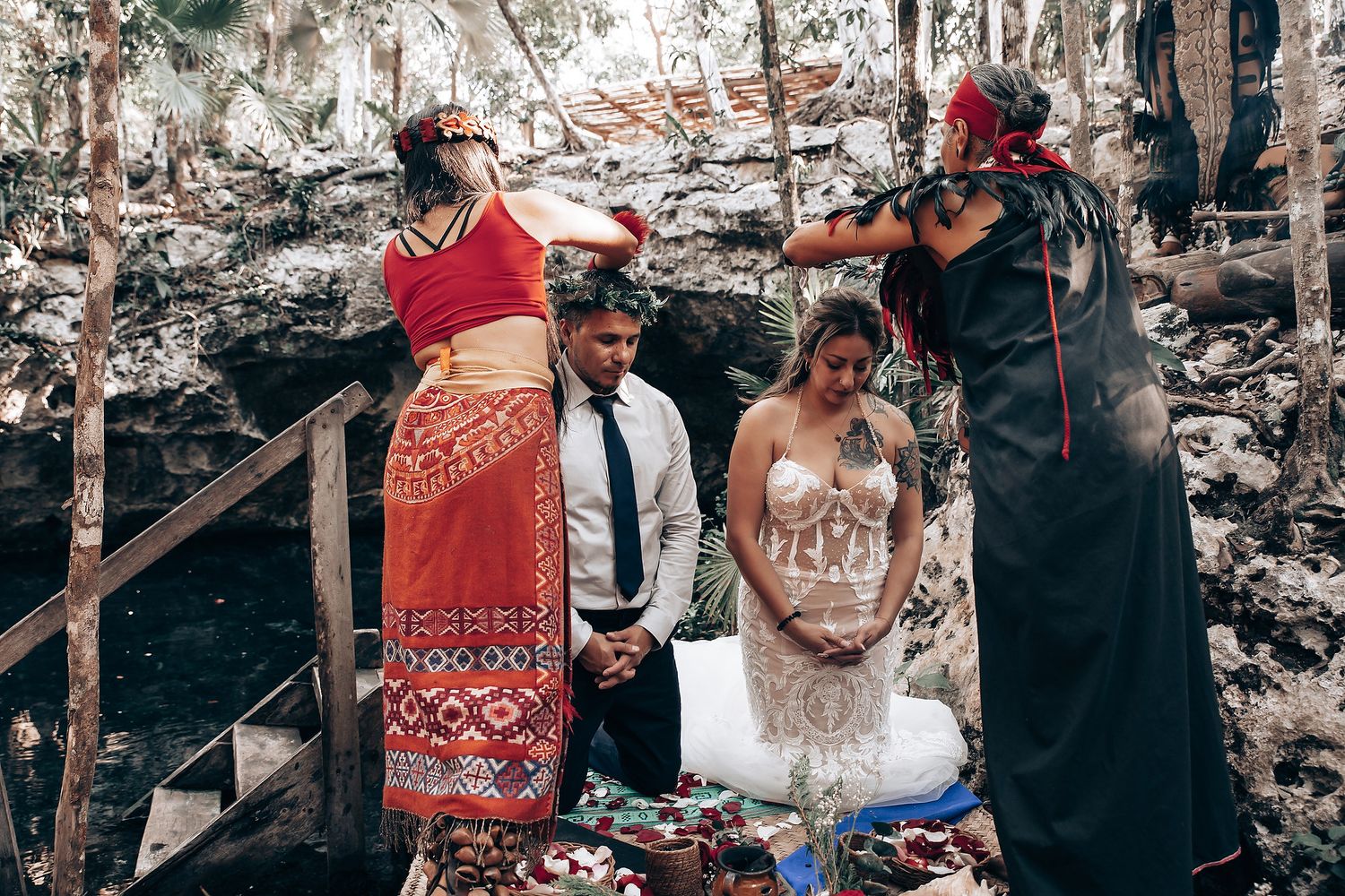 Wedding guests gather in a mystical cenote cave decorated with scattered rose petals and natural light.