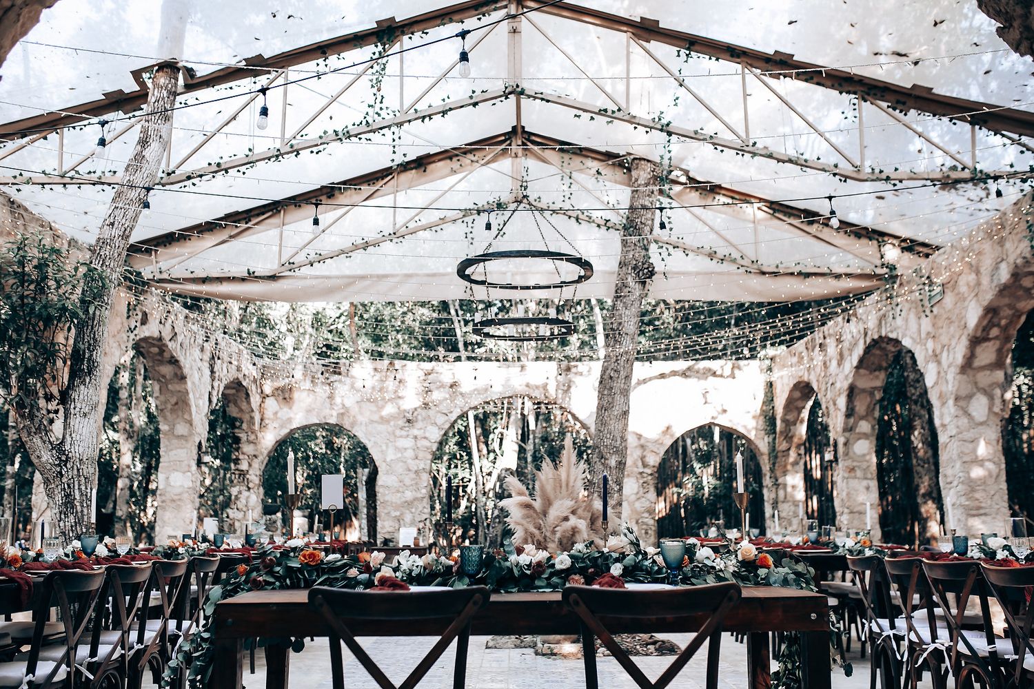 Elegant outdoor wedding ceremony setup with white chairs and hanging lights under a clear tent canopy.