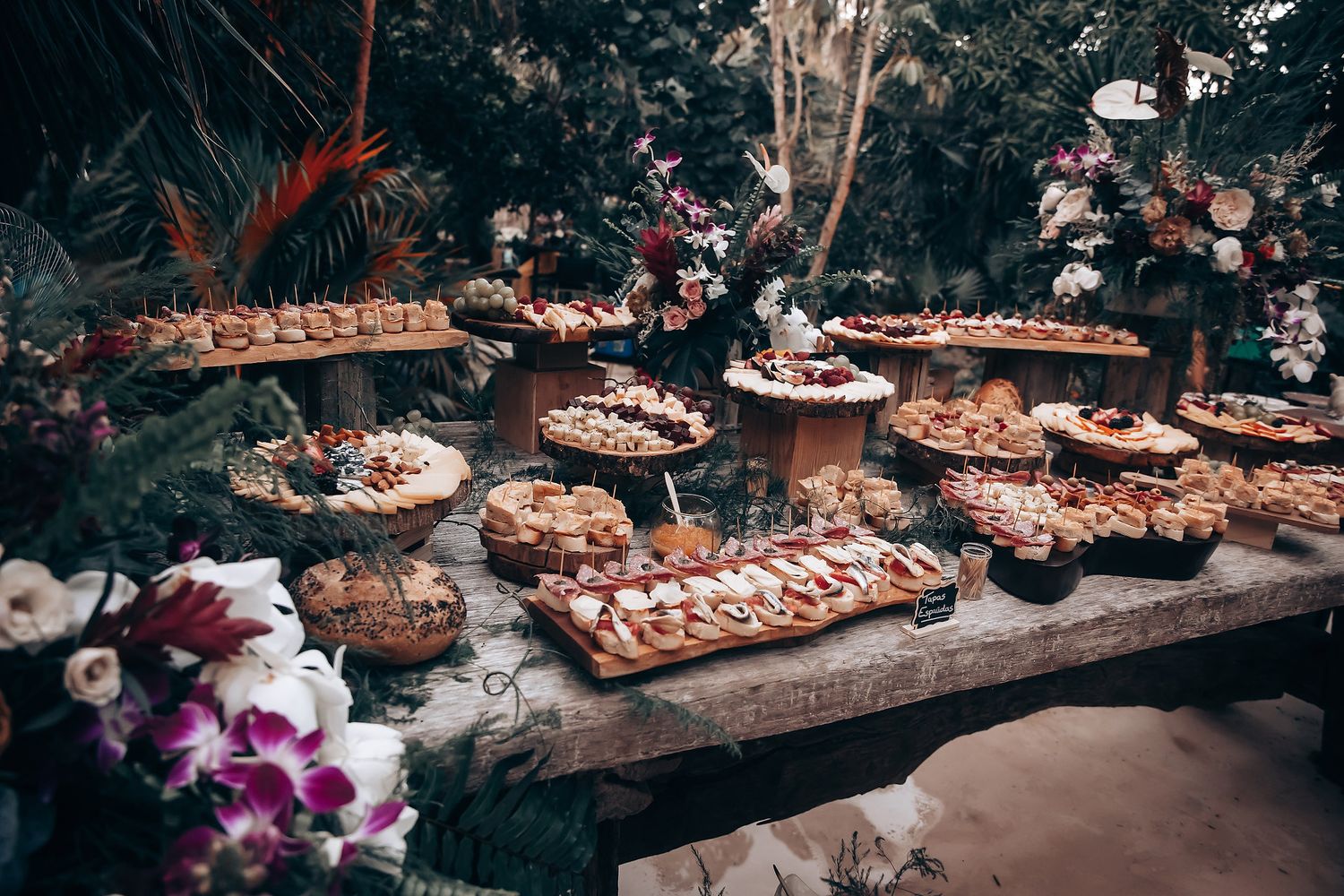 Long table filled with elegant desserts and pastries at an outdoor wedding reception.