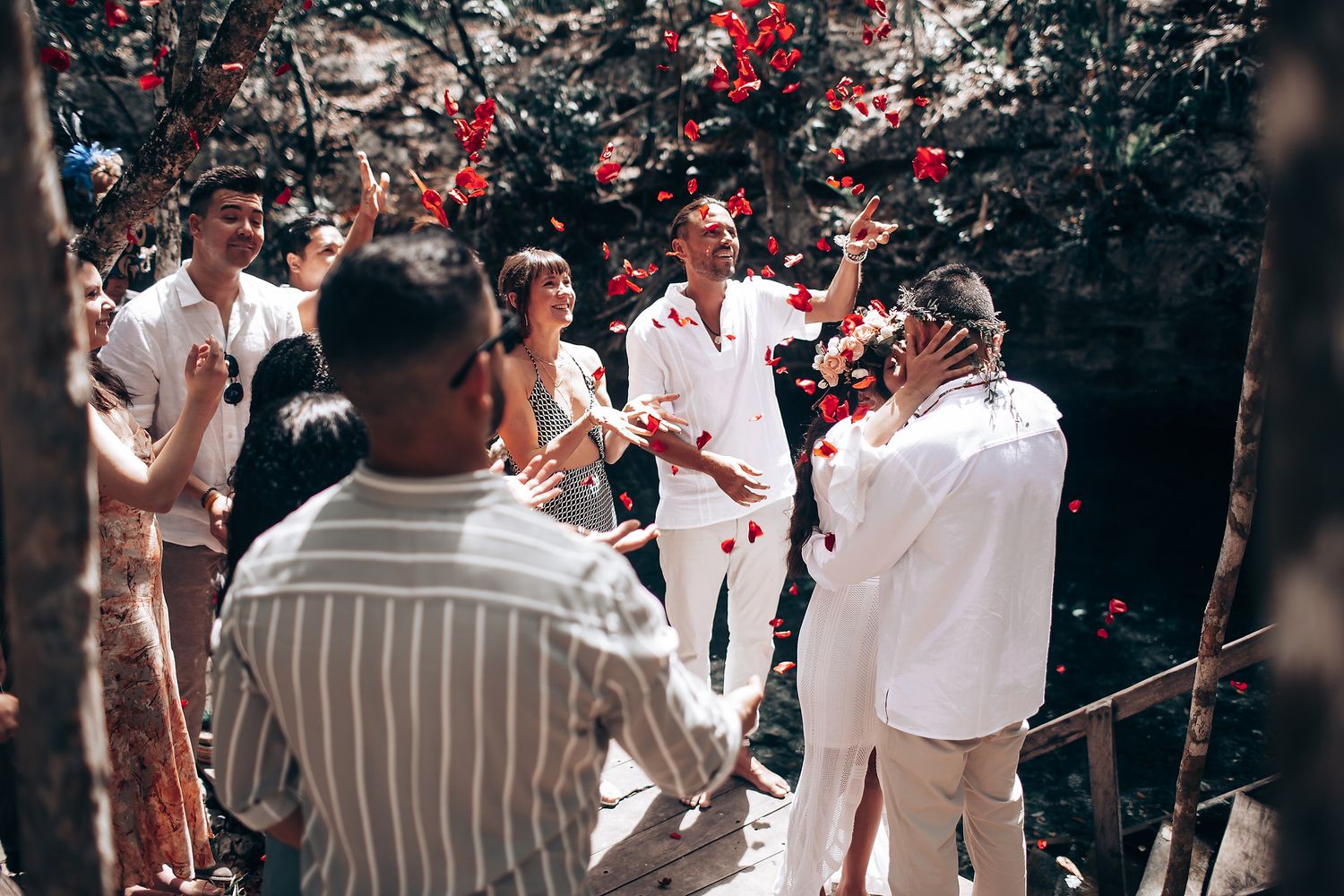 Traditional ceremony participants in white clothing gathered among trees with red decorative elements.