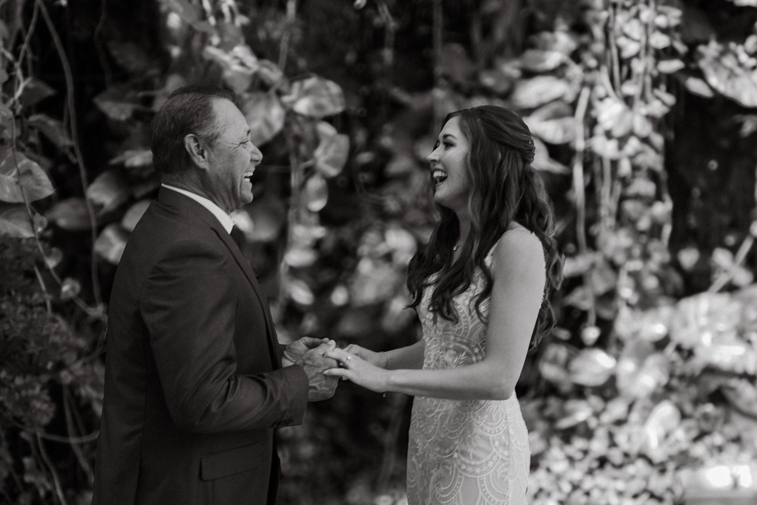 Emotional black and white first look moment between groom and bride holding hands before tropical garden wedding ceremony.