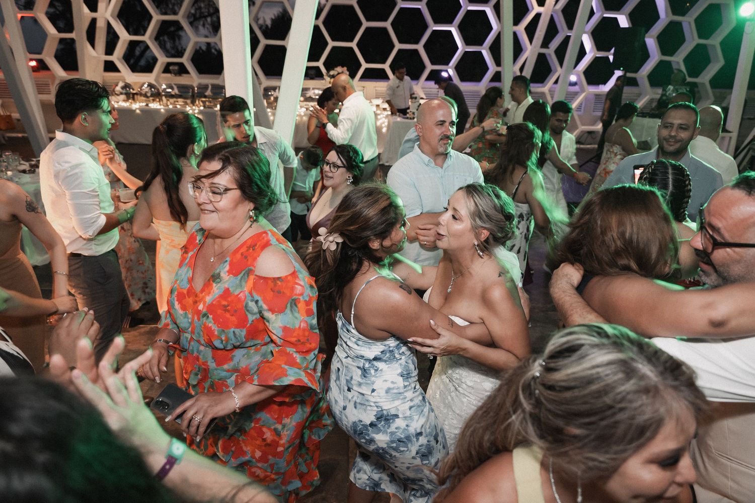 Guests dancing and celebrating joyfully under green lights at a lively outdoor wedding reception.
