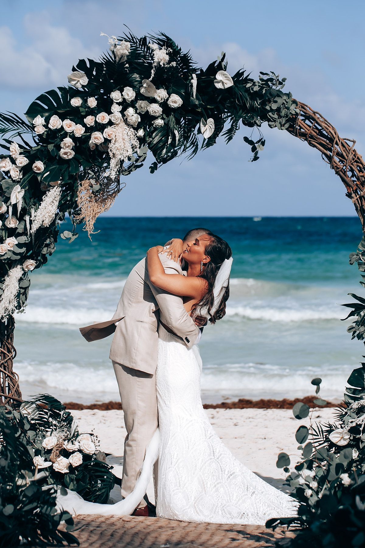 Beach wedding ceremony under floral arch with ocean waves in background.