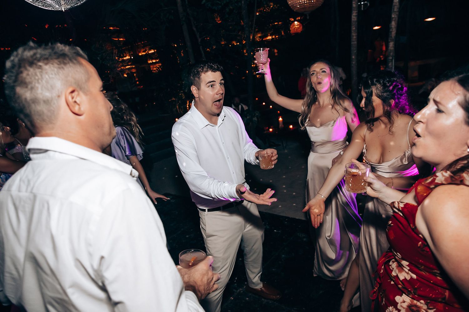 Wedding reception guests dancing and celebrating on a dimly lit dance floor.