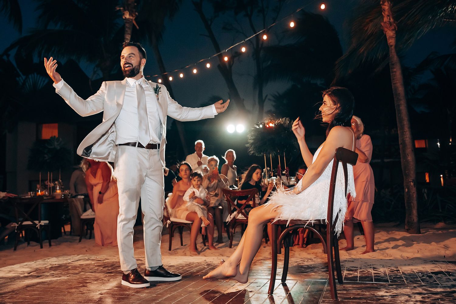 A lively dance moment under string lights at an outdoor evening wedding reception.