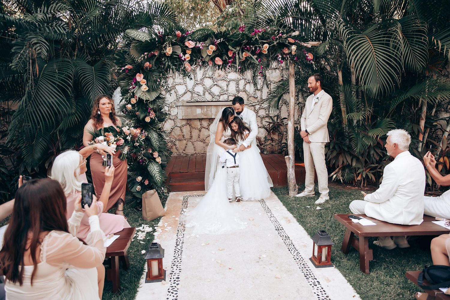 Elegant outdoor wedding reception with guests seated at decorated tables among tropical landscaping.