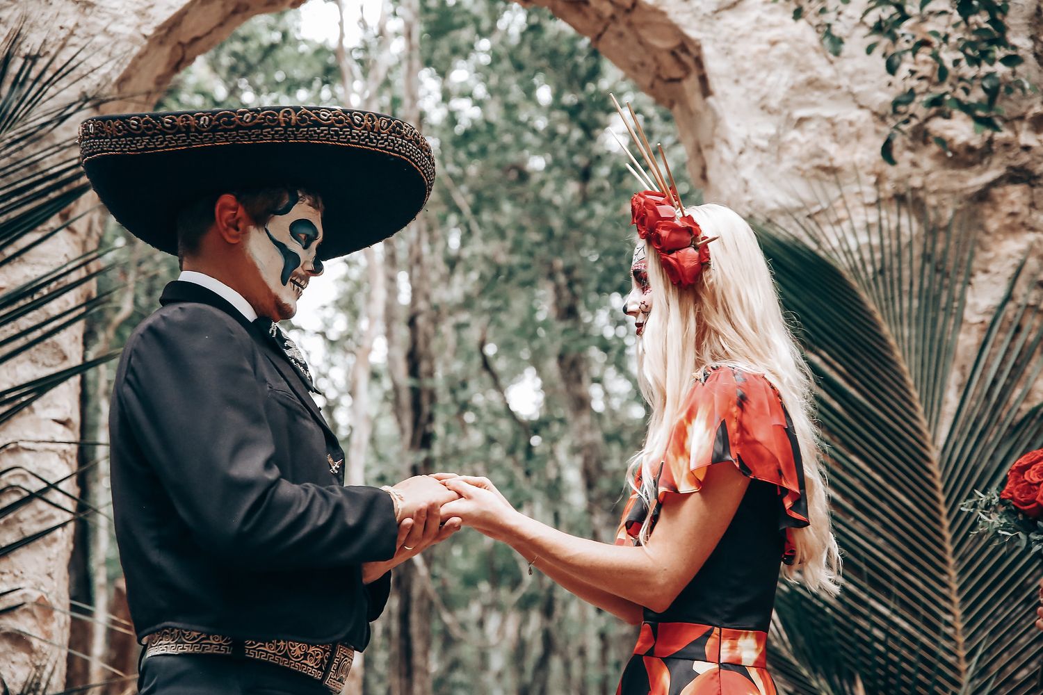 Couple in Day of the Dead makeup exchanging rings during an outdoor ceremony.