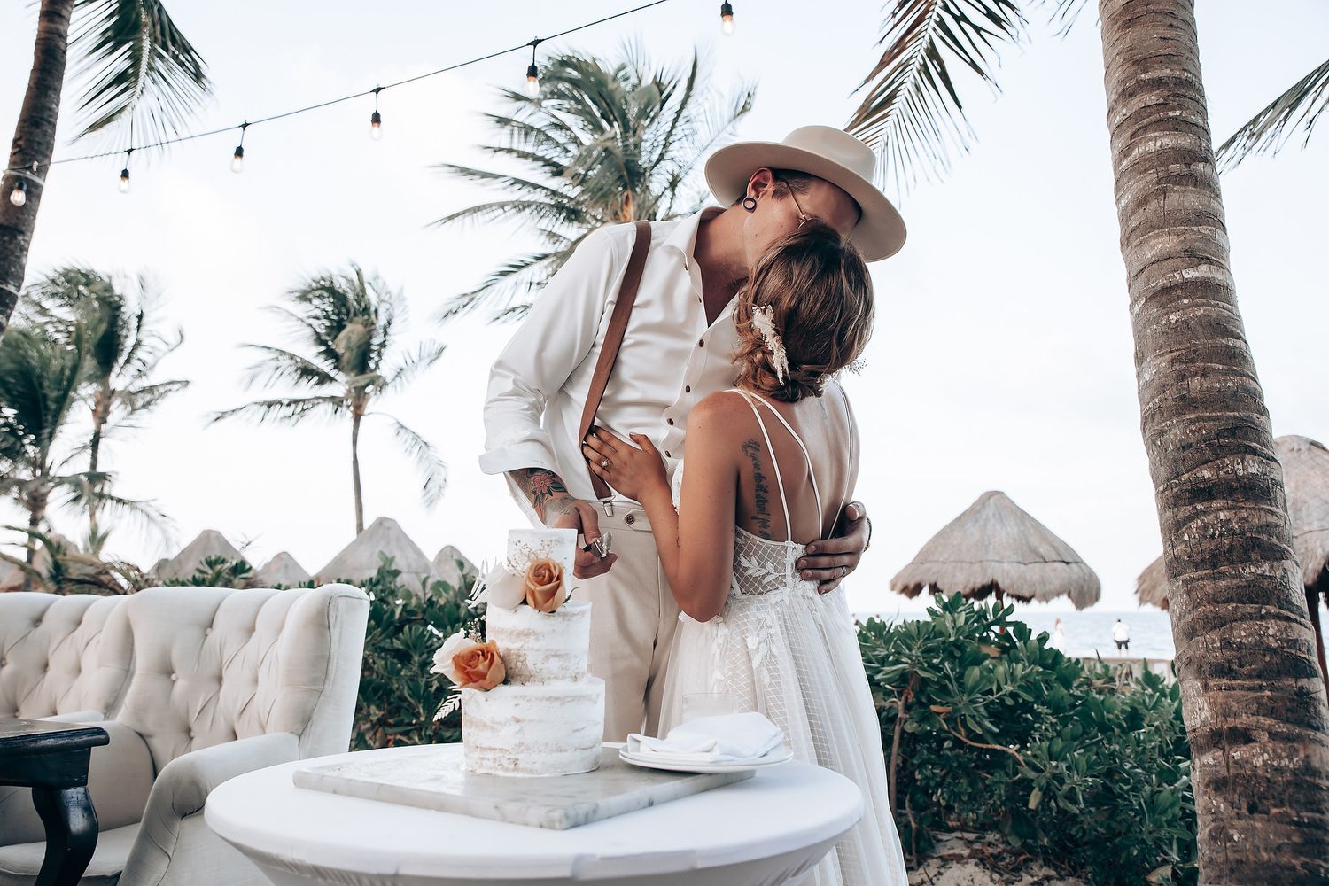 Newlyweds share a romantic moment at an outdoor reception with string lights and palm trees.