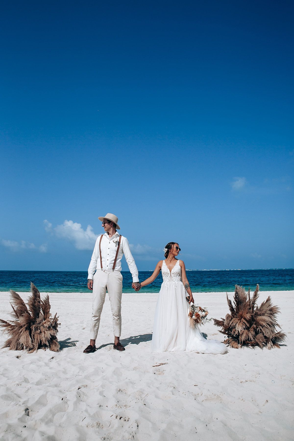 Romantic beach wedding photoshoot with dried palm arrangements on white sand.