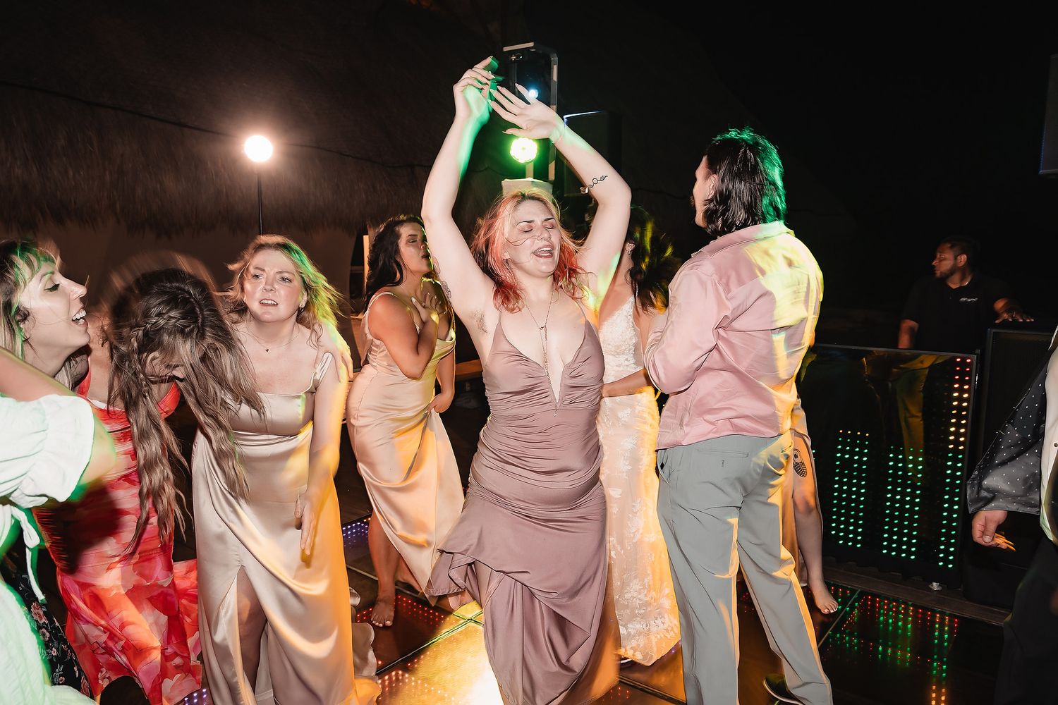 Women in elegant dresses dancing joyfully at a lively wedding reception party at night.