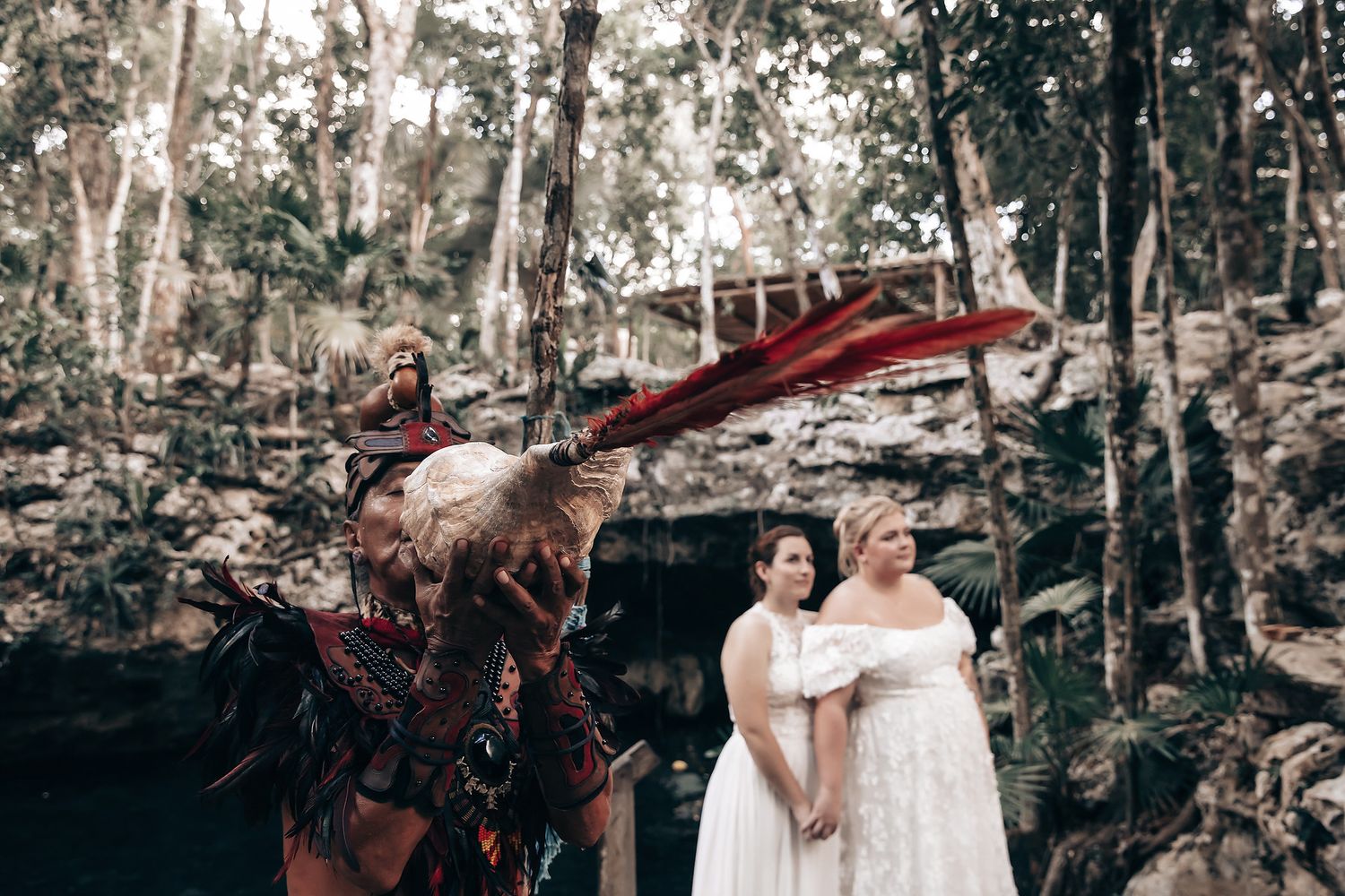 Two people in wedding attire standing in a lush, forested environment with a decorative arch and other elements.