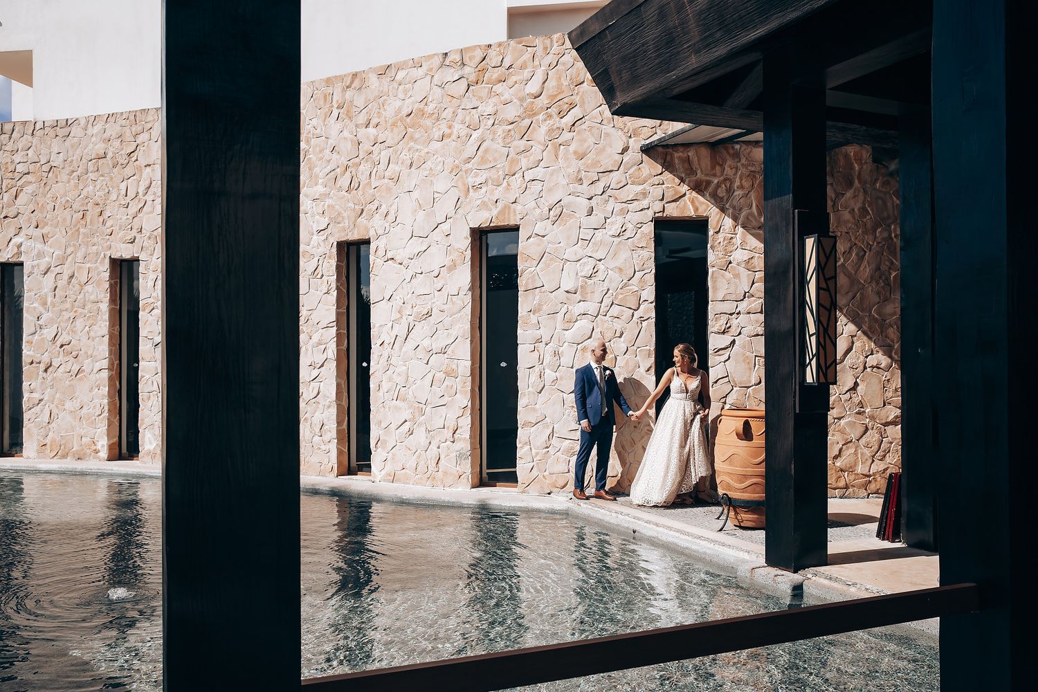 A couple walking together on a stone pathway near a pool in a tropical resort.