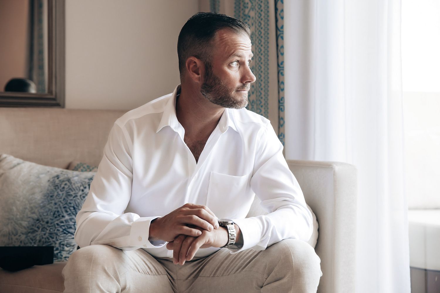 A man with a beard is sitting on a couch and looking thoughtfully.