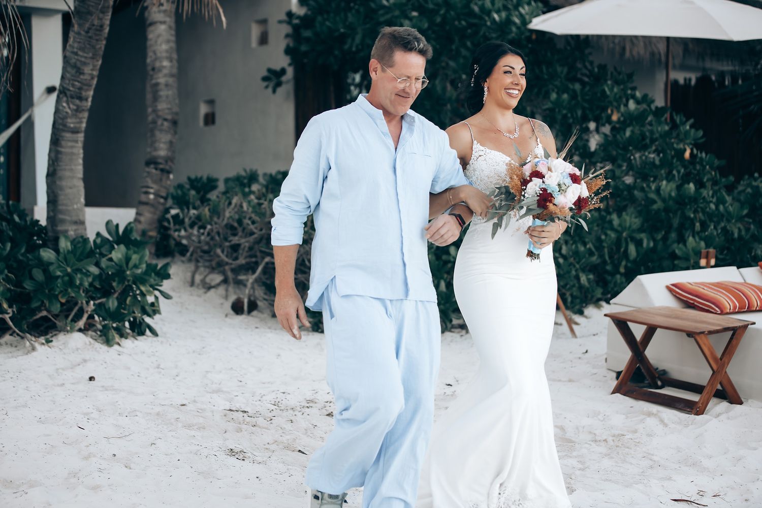 A wedding ceremony taking place on a beach, with a floral arch and guests in attendance.