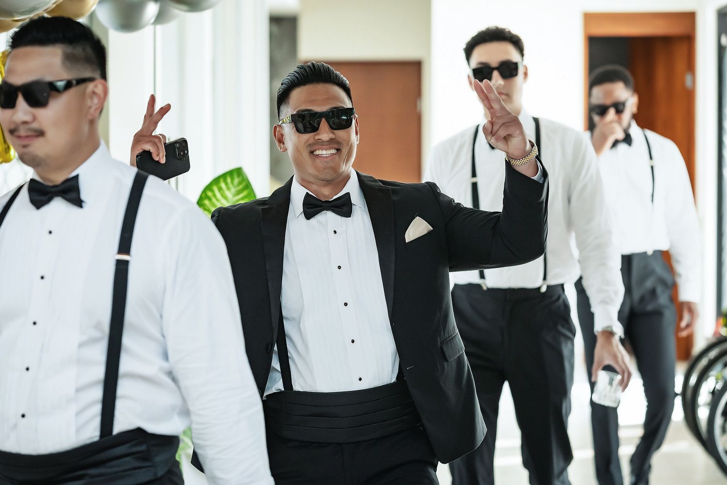 Group of men in black tuxedos and sunglasses smiling and posing outdoors at a formal event.
