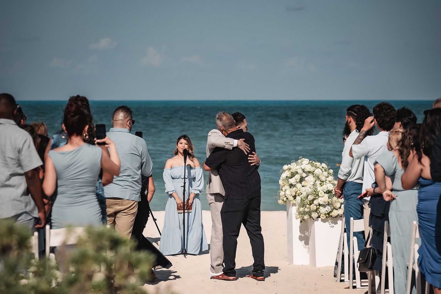 Emotional embrace during beachside wedding ceremony with ocean backdrop.
