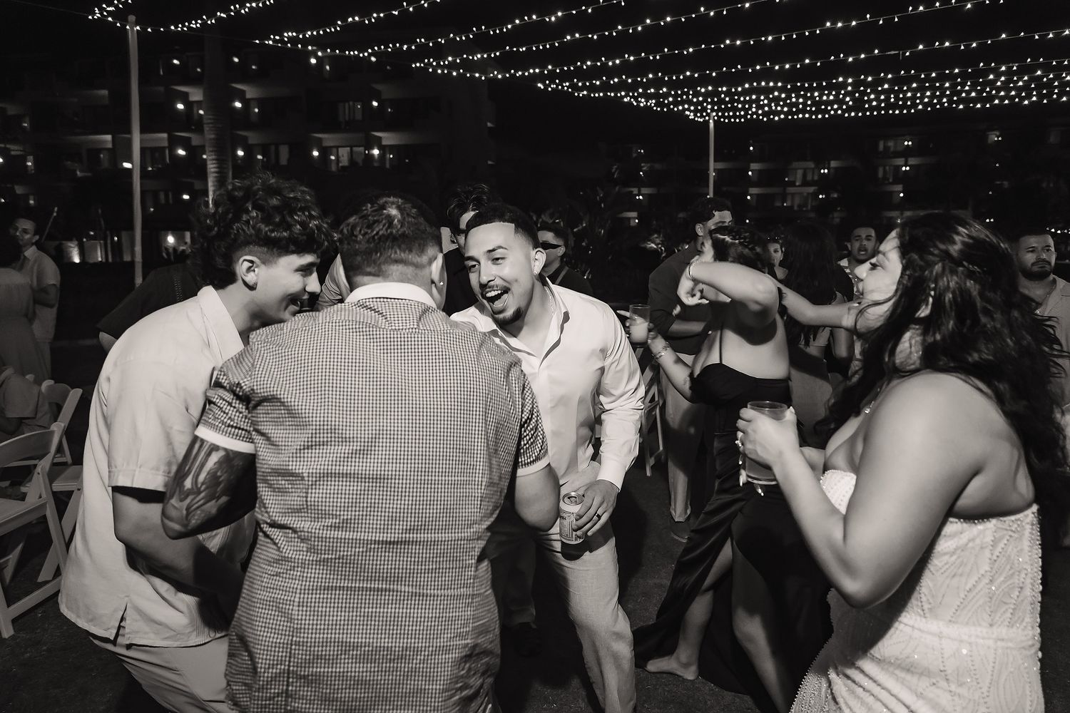 Black and white photo of guests dancing and laughing together at an outdoor evening wedding reception.