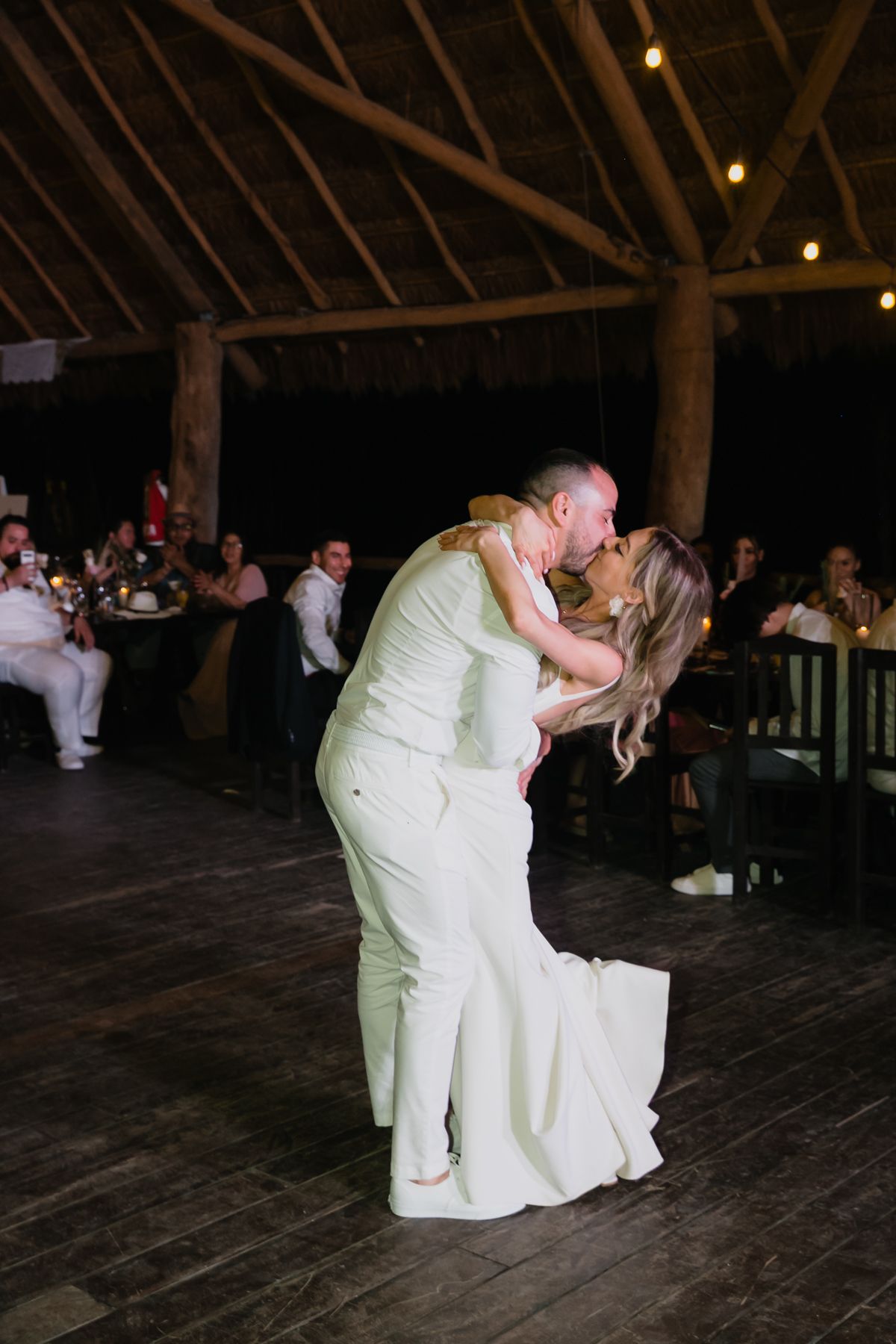Bride and groom sharing romantic dip kiss on dance floor during wedding reception.