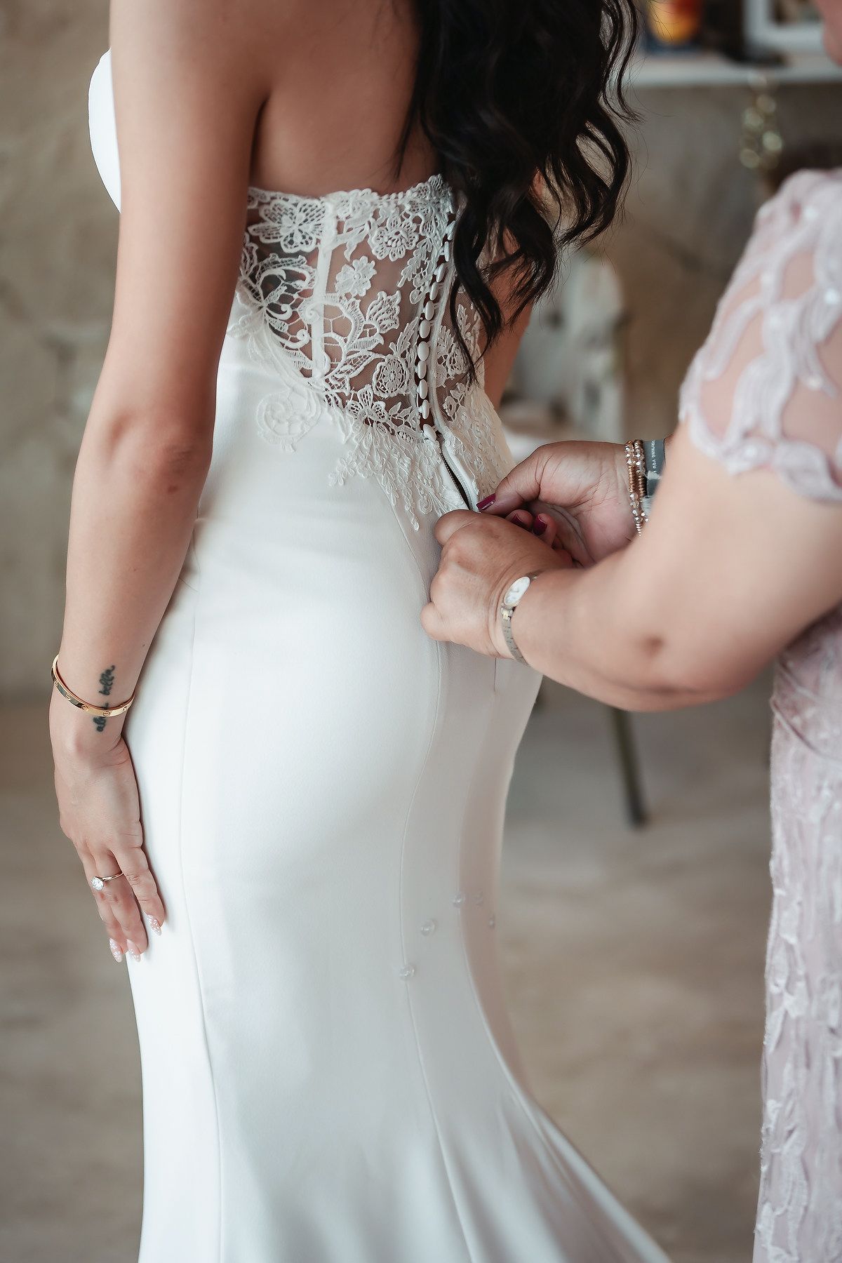 A bridesmaid fastening the back of a brides elegant white lace corset wedding gown.