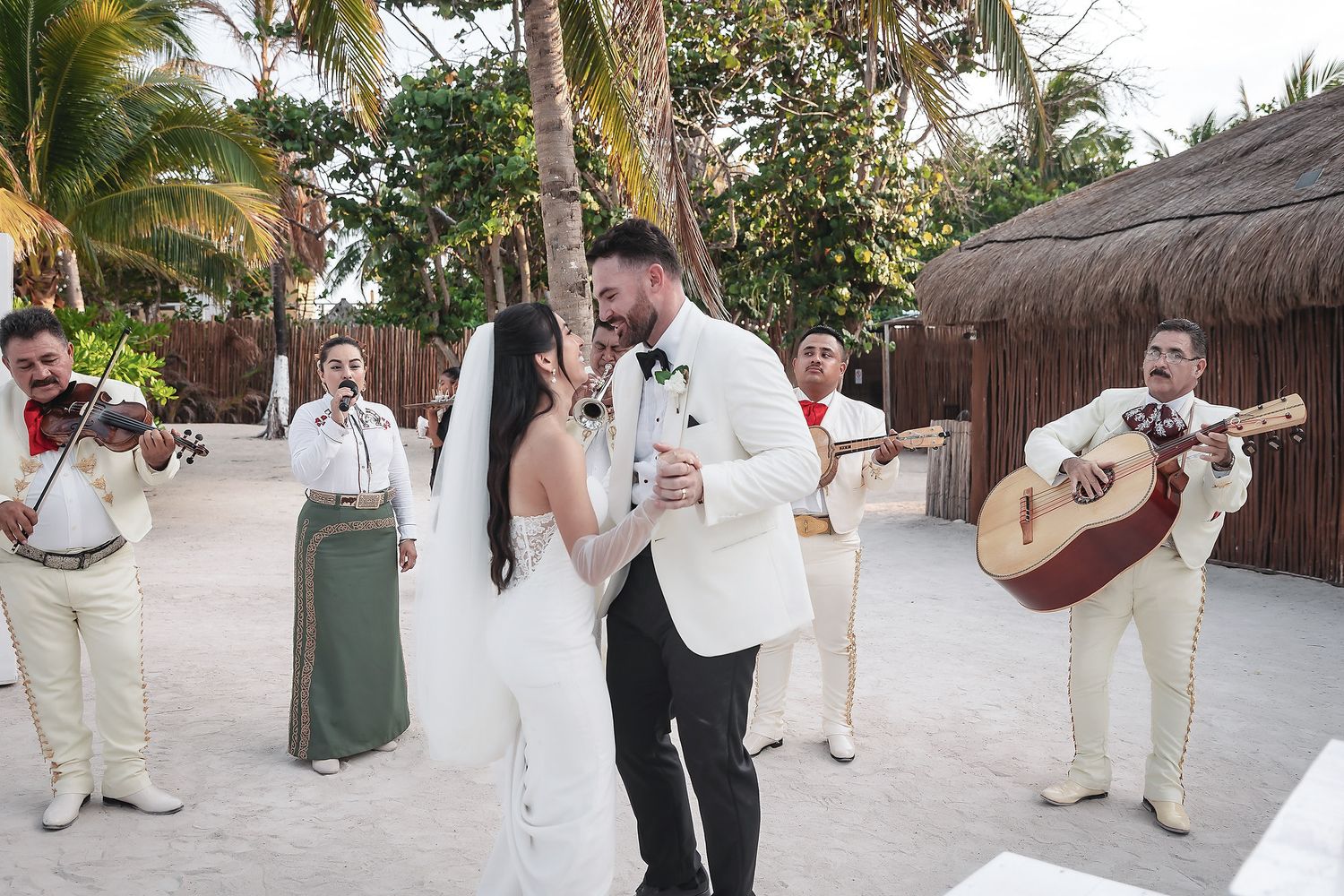 Bride and groom share first dance on beach with mariachi band performing at outdoor wedding ceremony in tropical resort.