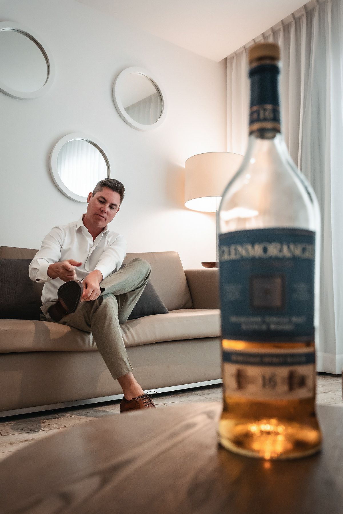 Groom putting on shoes beside a Glenmorangie whisky bottle in a modern hotel suite.