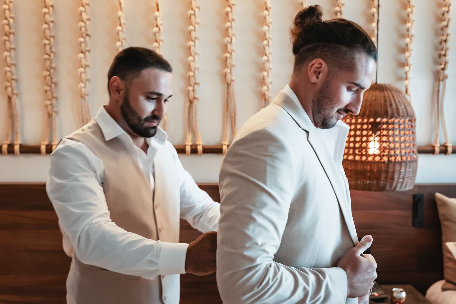 Two grooms in elegant suits prepare for their wedding ceremony, one adjusting the other's jacket.