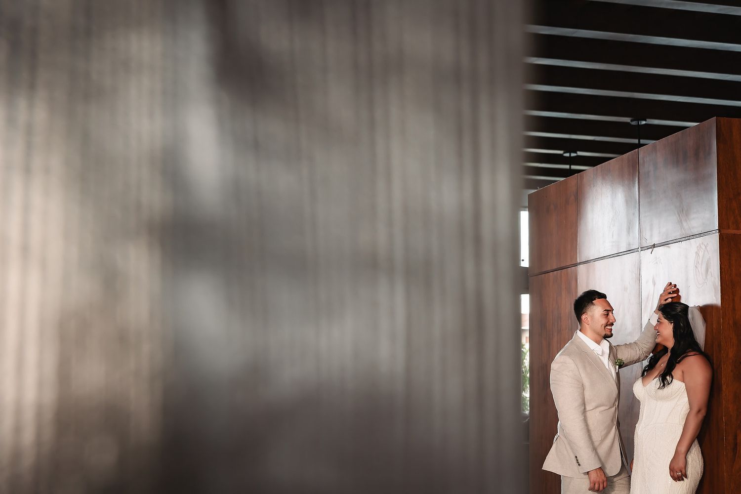 Bride and groom share a romantic moment framed by modern architecture with warm wood and metal panels.