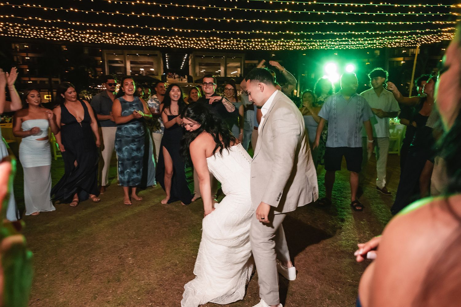 Bride and groom share a lively dance surrounded by cheering guests under string lights at outdoor wedding.