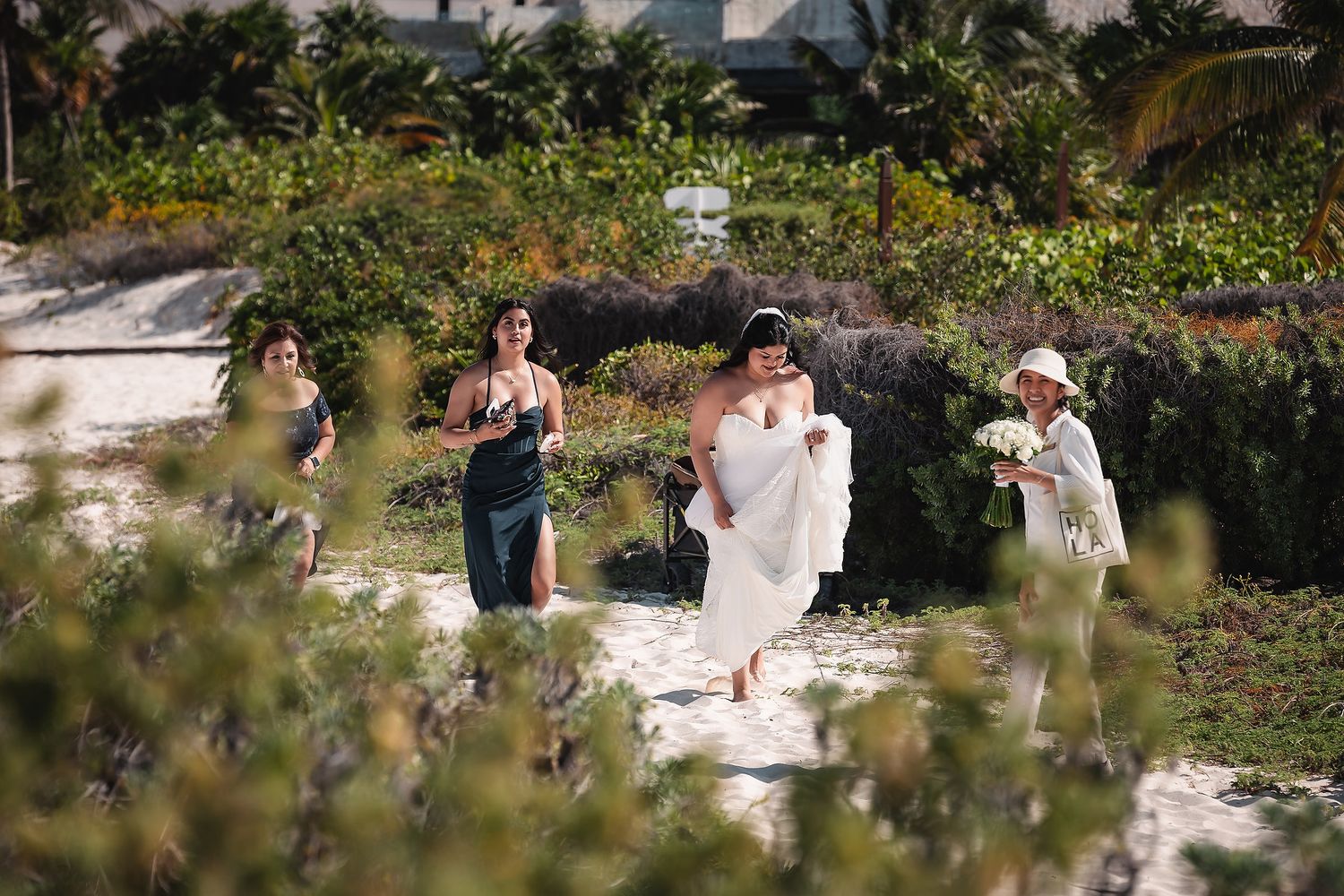 Bride and bridesmaids walking through tropical greenery at a beach wedding.