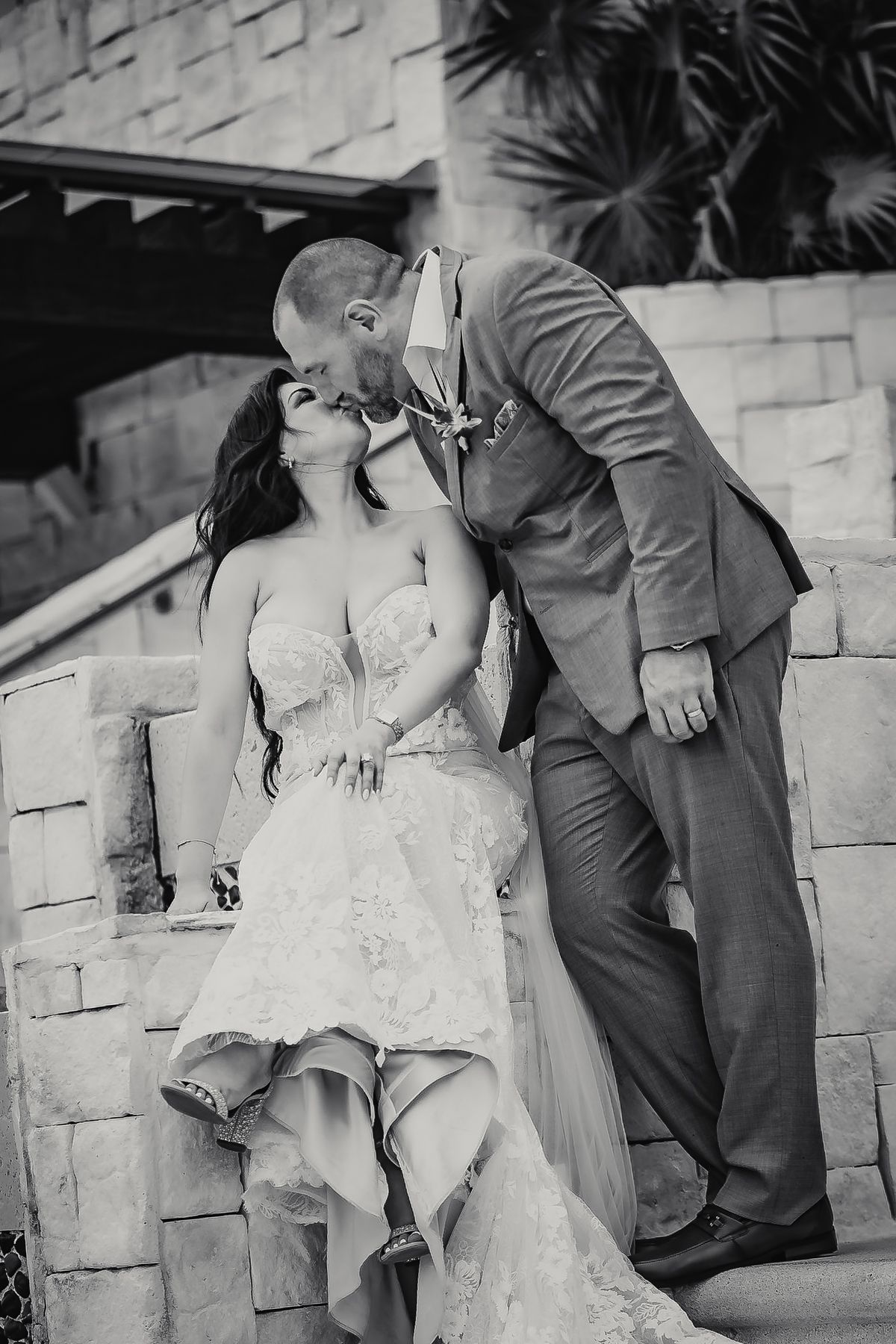 Black and white photo of a bride and groom sharing a romantic kiss on stone steps at their wedding.
