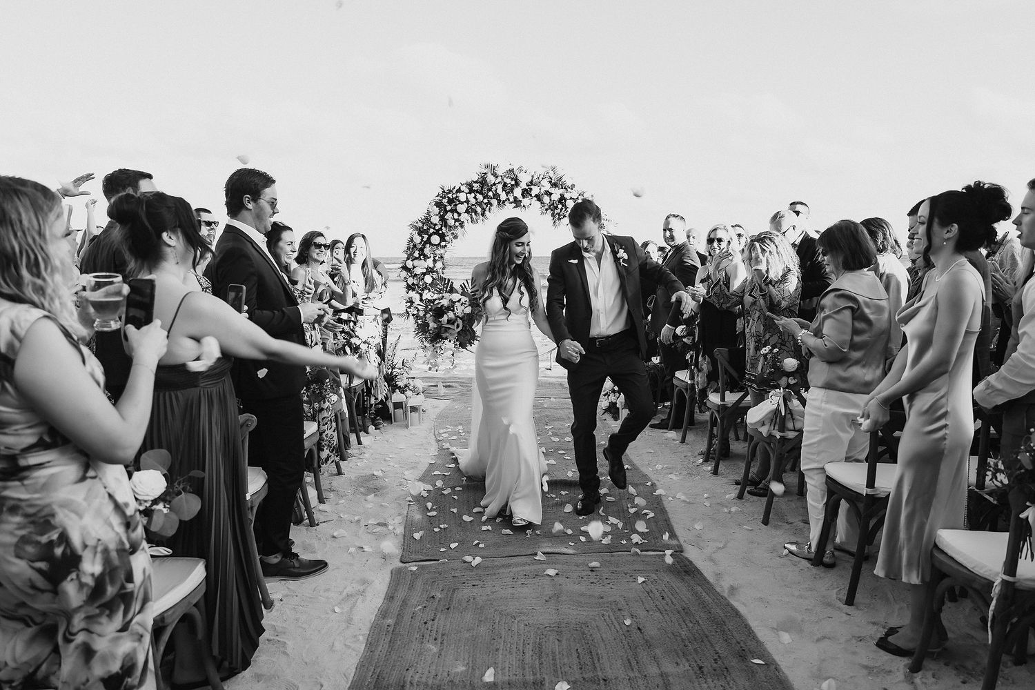 Black and white photo of a joyful couple walking down the aisle after their outdoor wedding ceremony.