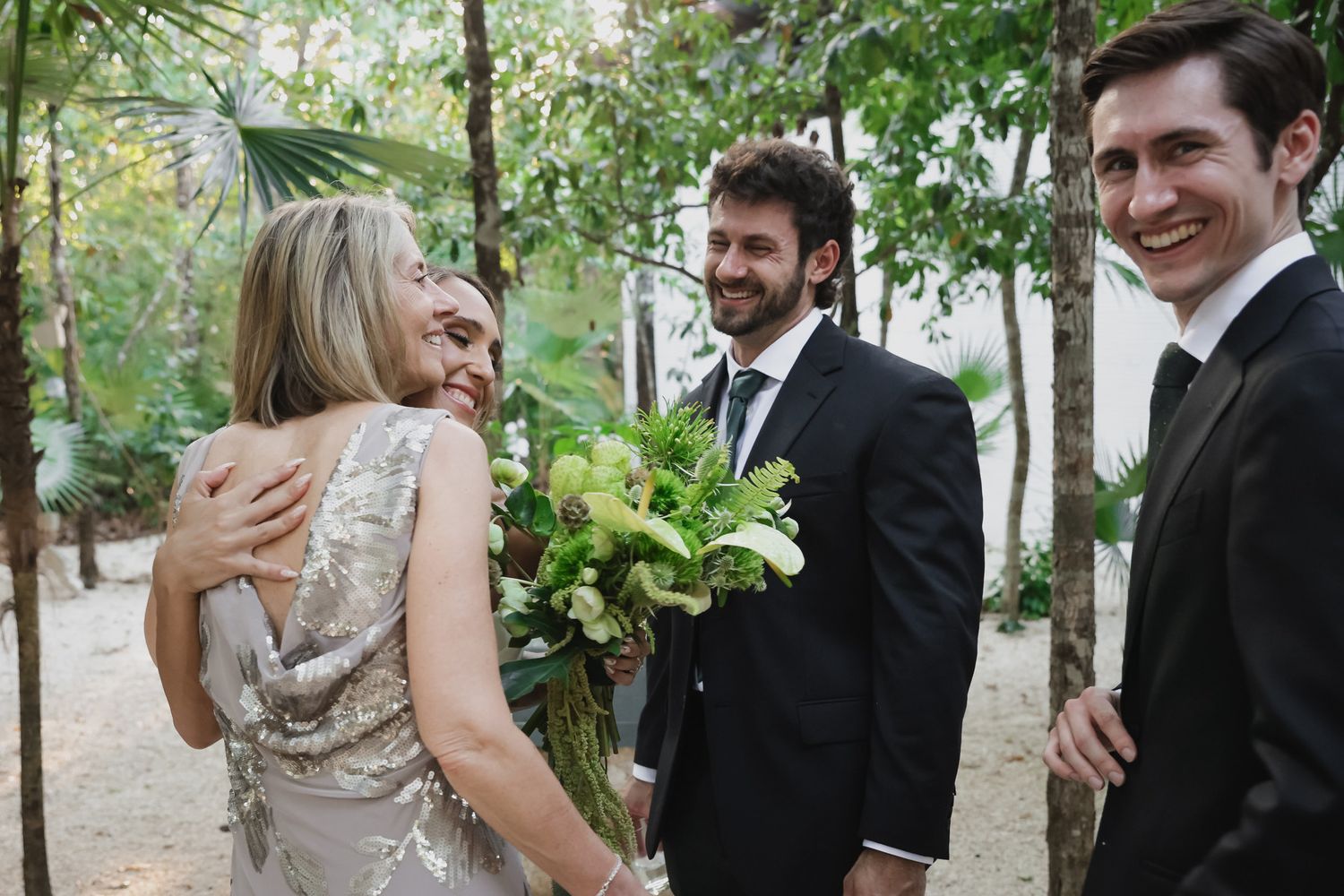 Bride and groom smiling with guests at an outdoor wedding, bride holding a lush green bouquet.