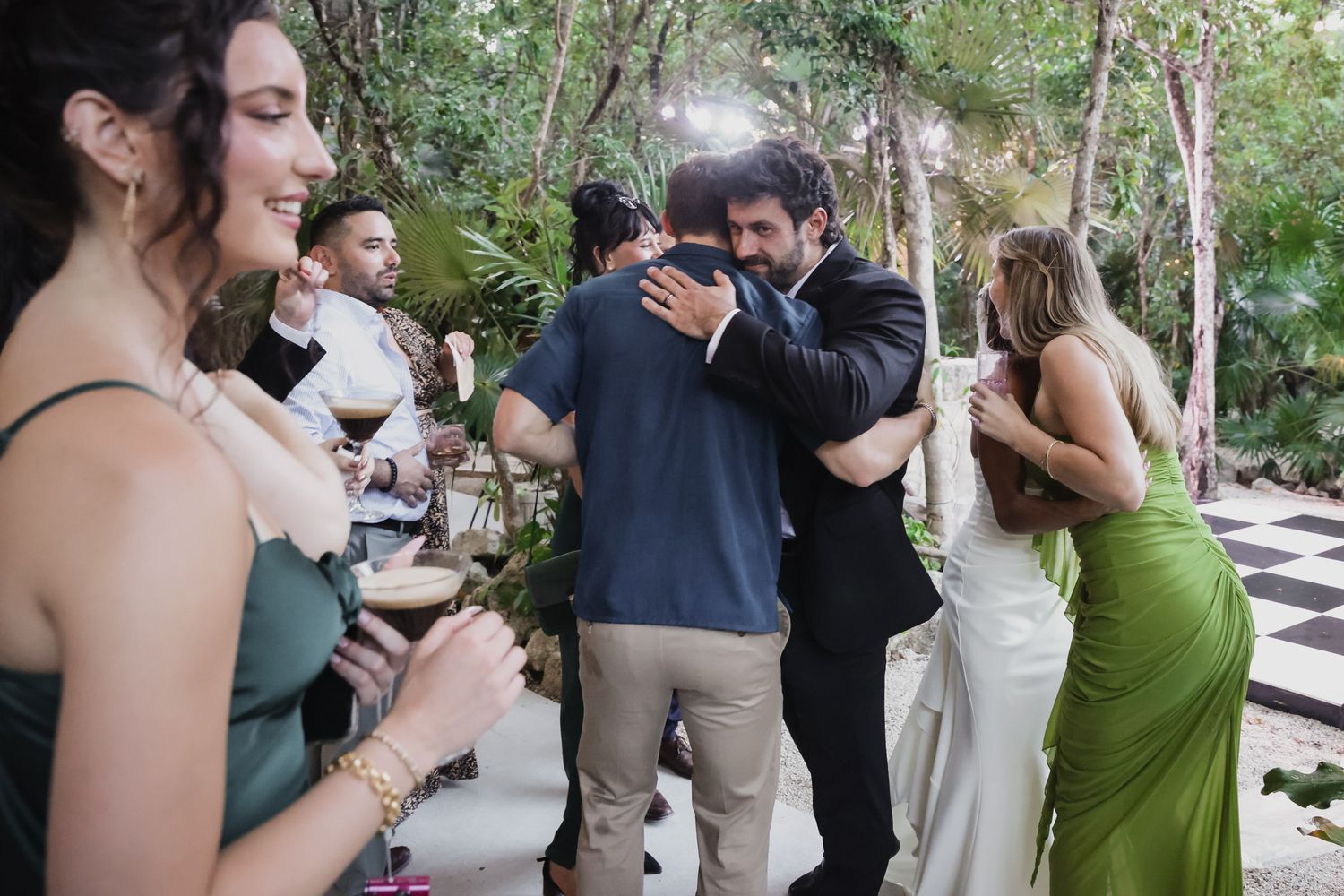 Guests hugging and socializing at an outdoor wedding reception surrounded by tropical greenery.