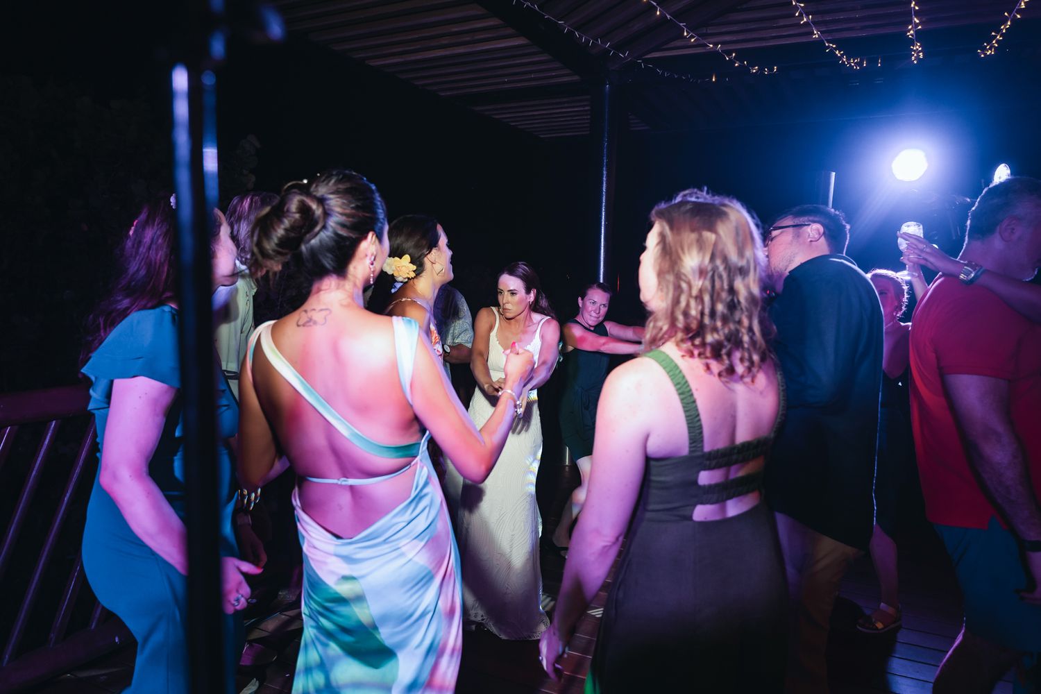 Guests dancing at a wedding reception party under colorful lights on an outdoor dance floor at night.