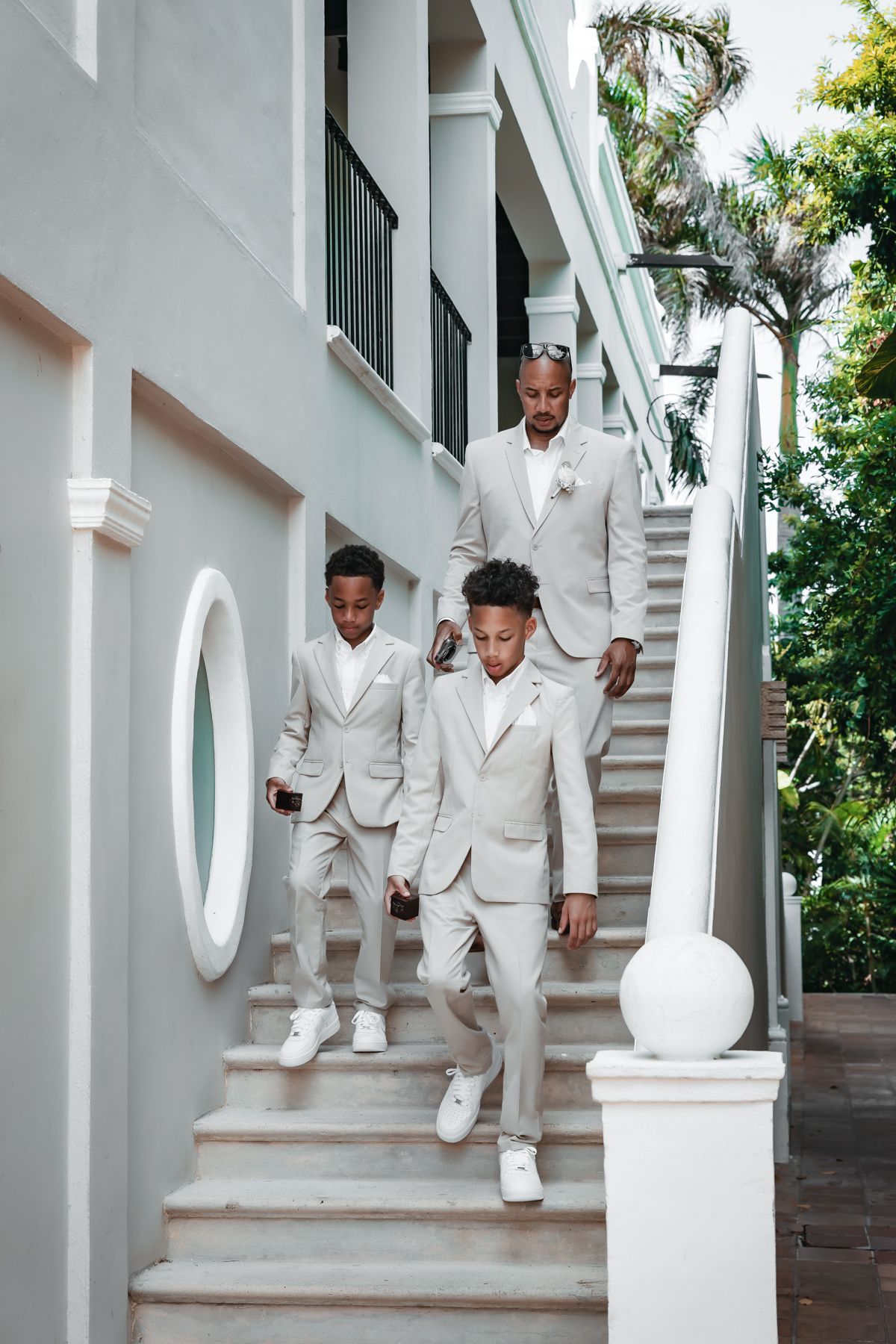 Man and two boys in matching light gray suits descend outdoor stairs at elegant venue.