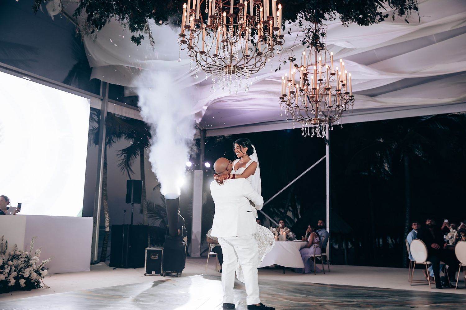 Wedding reception venue with elegant chandeliers and white draped ceiling creating magical atmosphere.