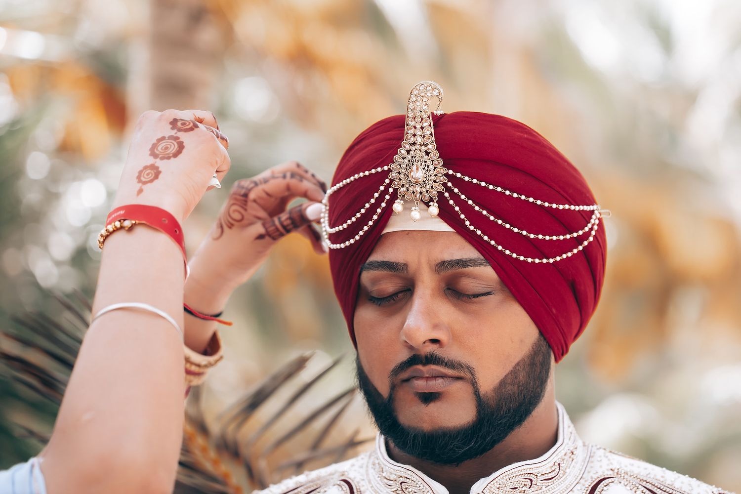 Ornate wedding ceremony details featuring traditional red turban and jeweled accessories.