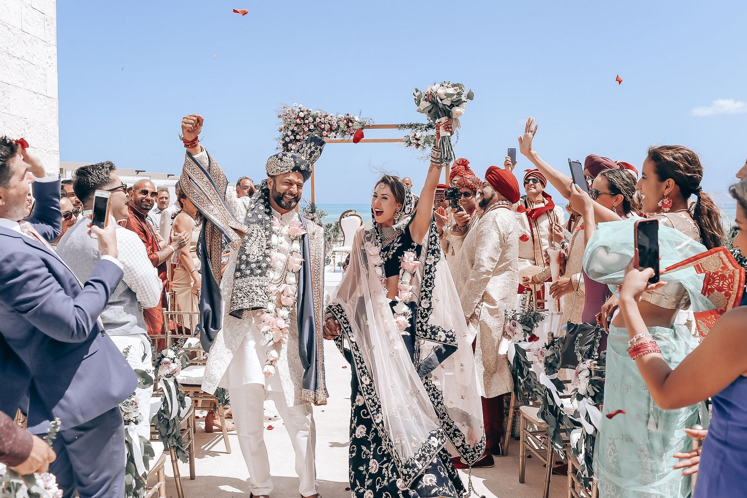 Wedding party and guests celebrate with confetti and rose petals during an outdoor ceremony.
