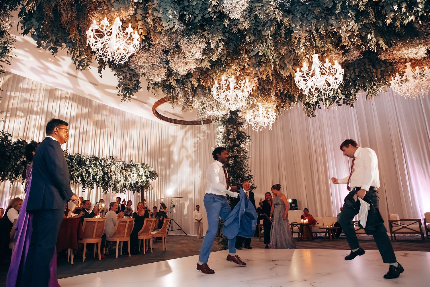 Elegant wedding reception venue with crystal chandeliers and greenery decorations hanging from the ceiling.